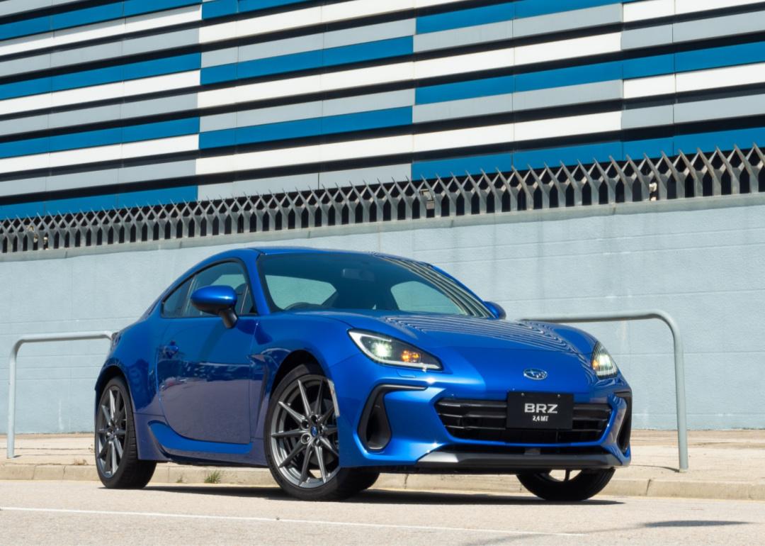 A blue Subaru BRZ is parked in front of a modern blue and gray building.