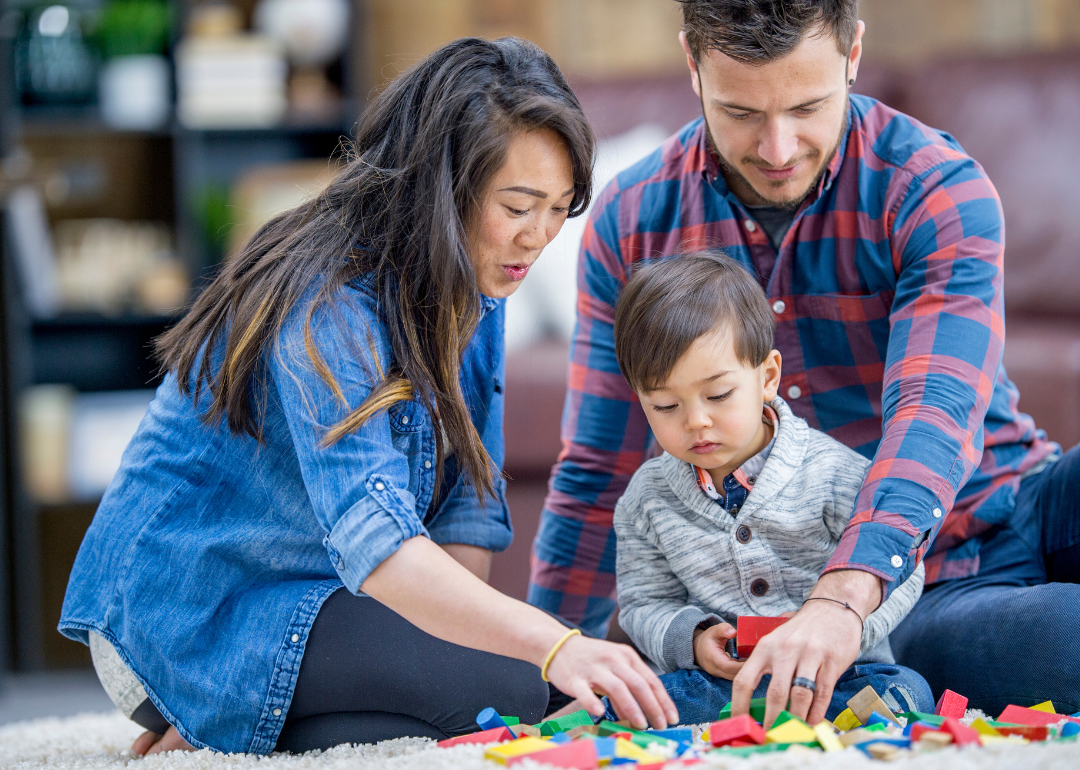 A young child arranges colorful blocks with his parents on the floor.