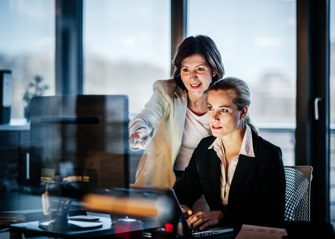 Two women work in a corporate office in front of a computer.