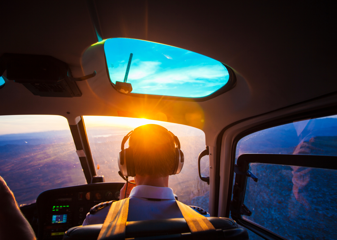 Pilot sitting in an airplane cockpit overlooking the clouds.