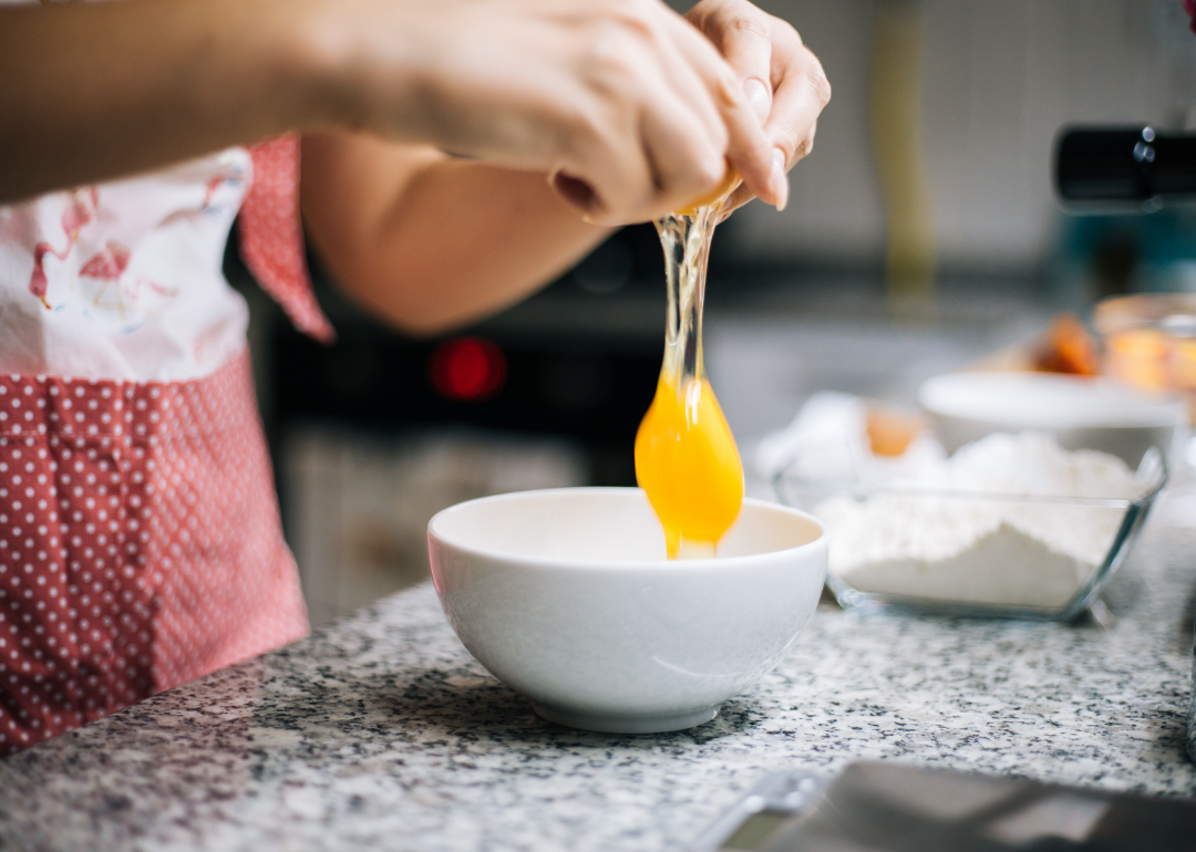 An egg yolk is dropped into a white bowl from a cracked shell.