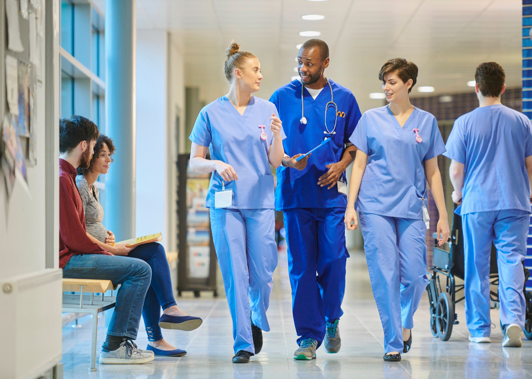 Three nurses make their way along a hospital corridor while talking.