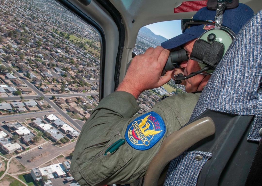 Officer using binoculars in a police helicopter over Phoenix.
