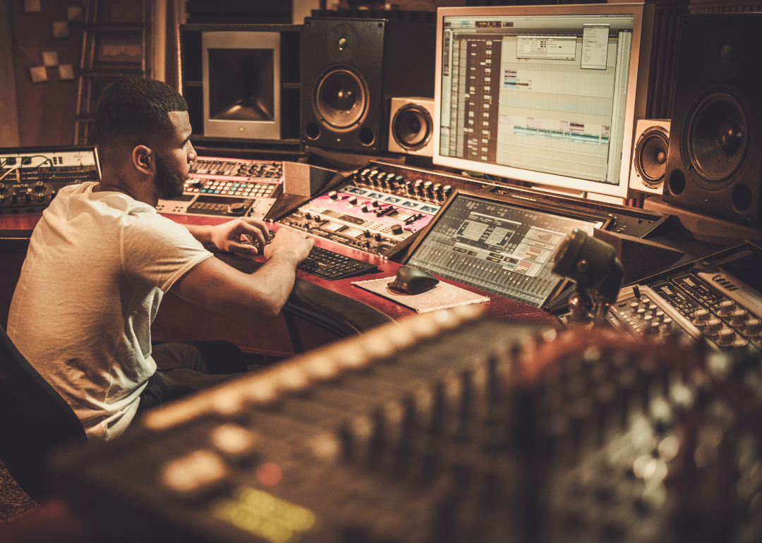 A sound engineer sits in a recording book surrounded by equipment.