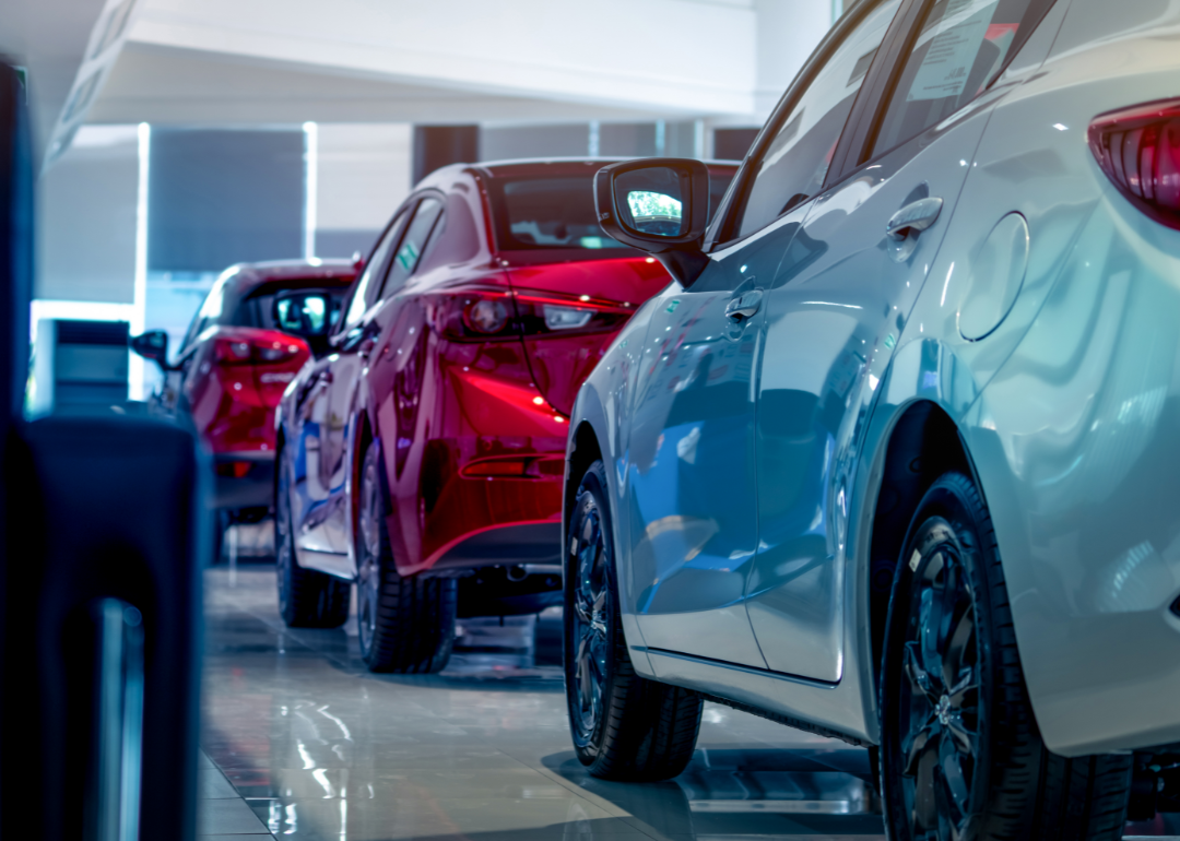 Three new cars are parked inside an auto dealership.