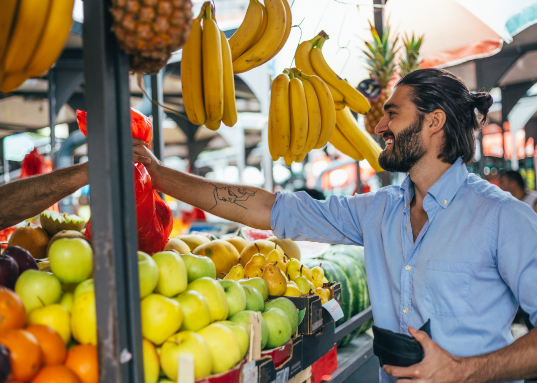 A man buys a bag of fruit at an outdoor farmer's market.