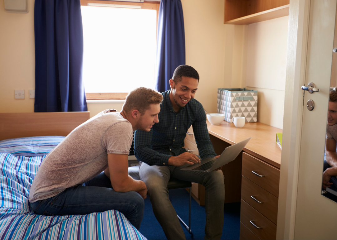 Two male students study a laptop together in their dorm room.