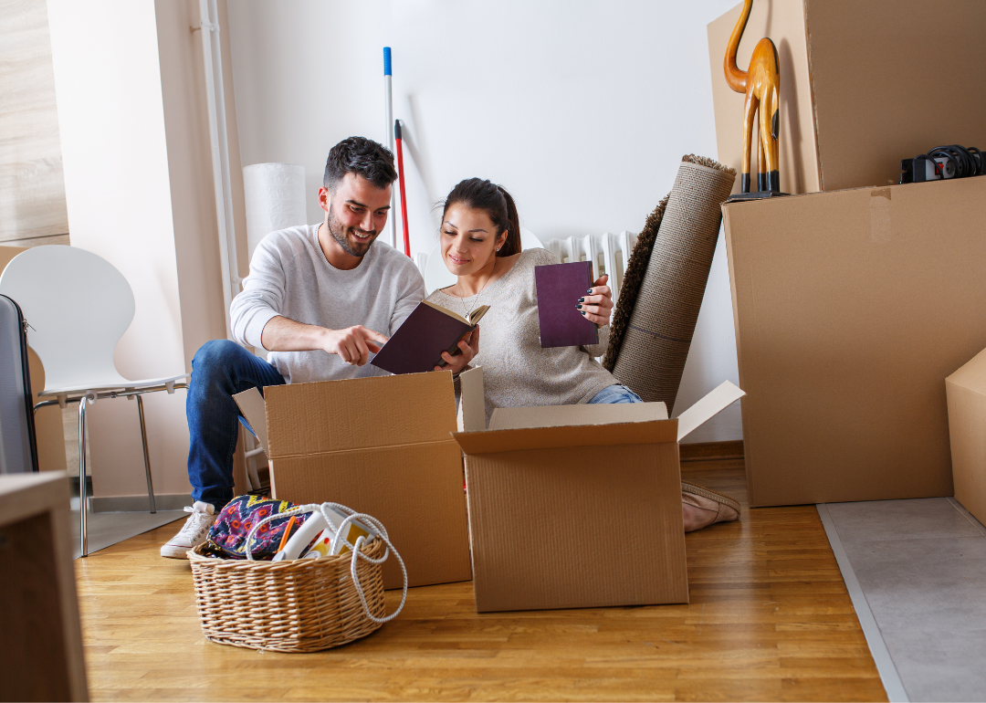 A couple sits in a living room opening moving boxes.