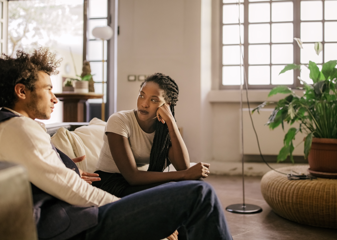 A young man and woman have a serious discussion in their apartment living room.