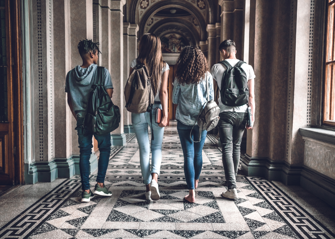 Four students walk away from the camera down an ornate corridor of a historic college.