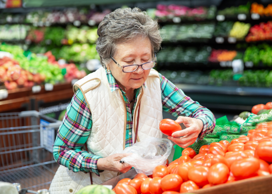 A senior woman inspects the ripeness of tomatoes in a market.