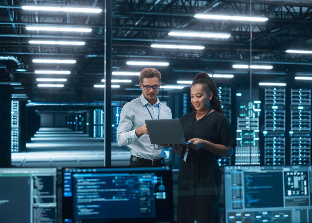 Two colleagues stand before multiple racks of servers supporting cloud computing.