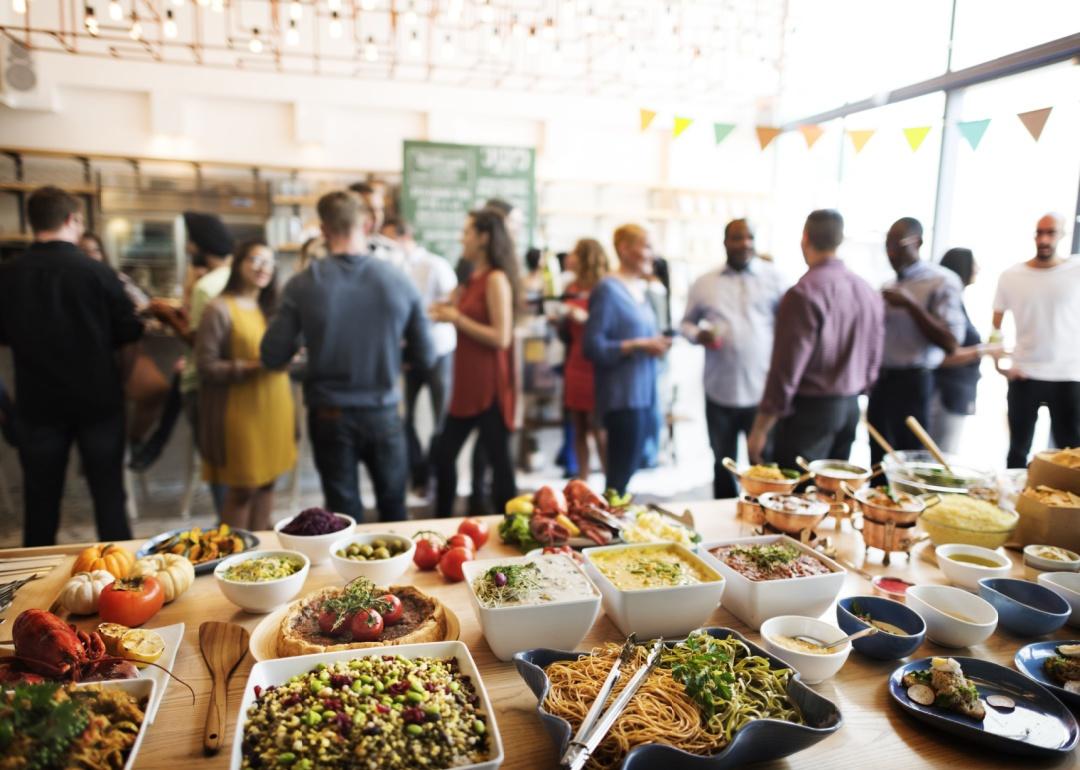 A table of buffet food with a party in the background.