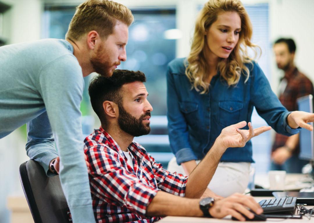 Three colleagues confer and study a program on a computer screen.