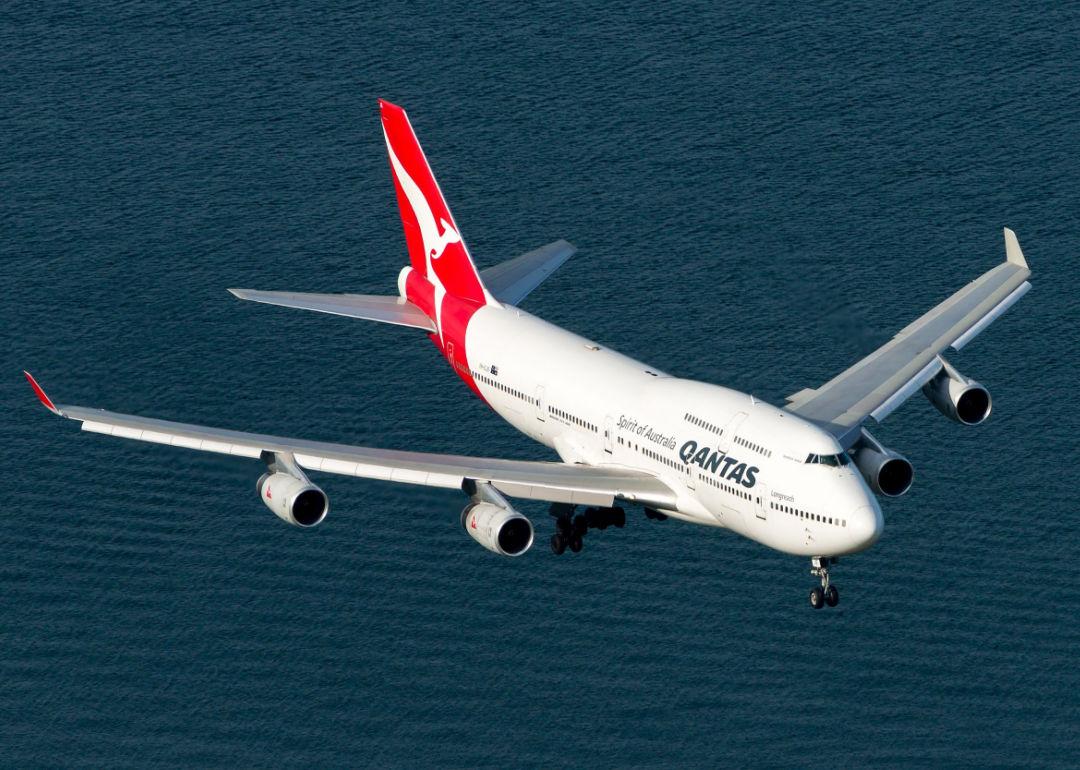 A Qantas jet seen from above flying over water.