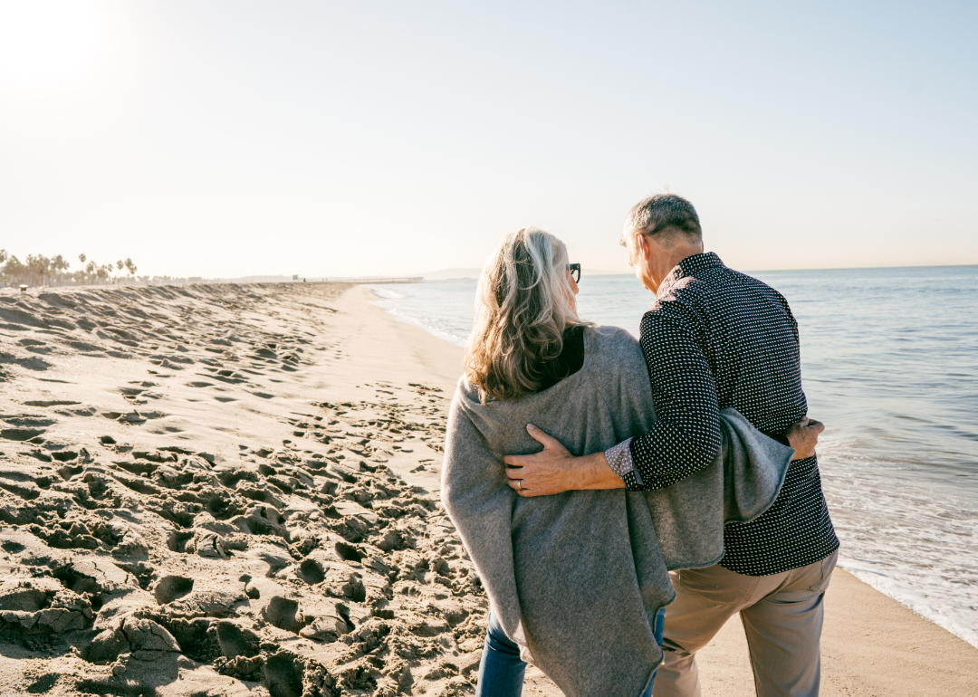 A couple walks together along a beach.