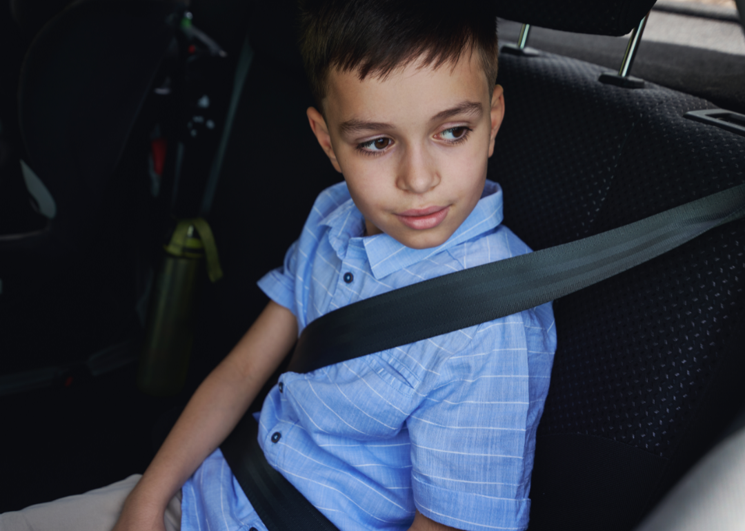 A child wearing a seat belt in the back of a car.
