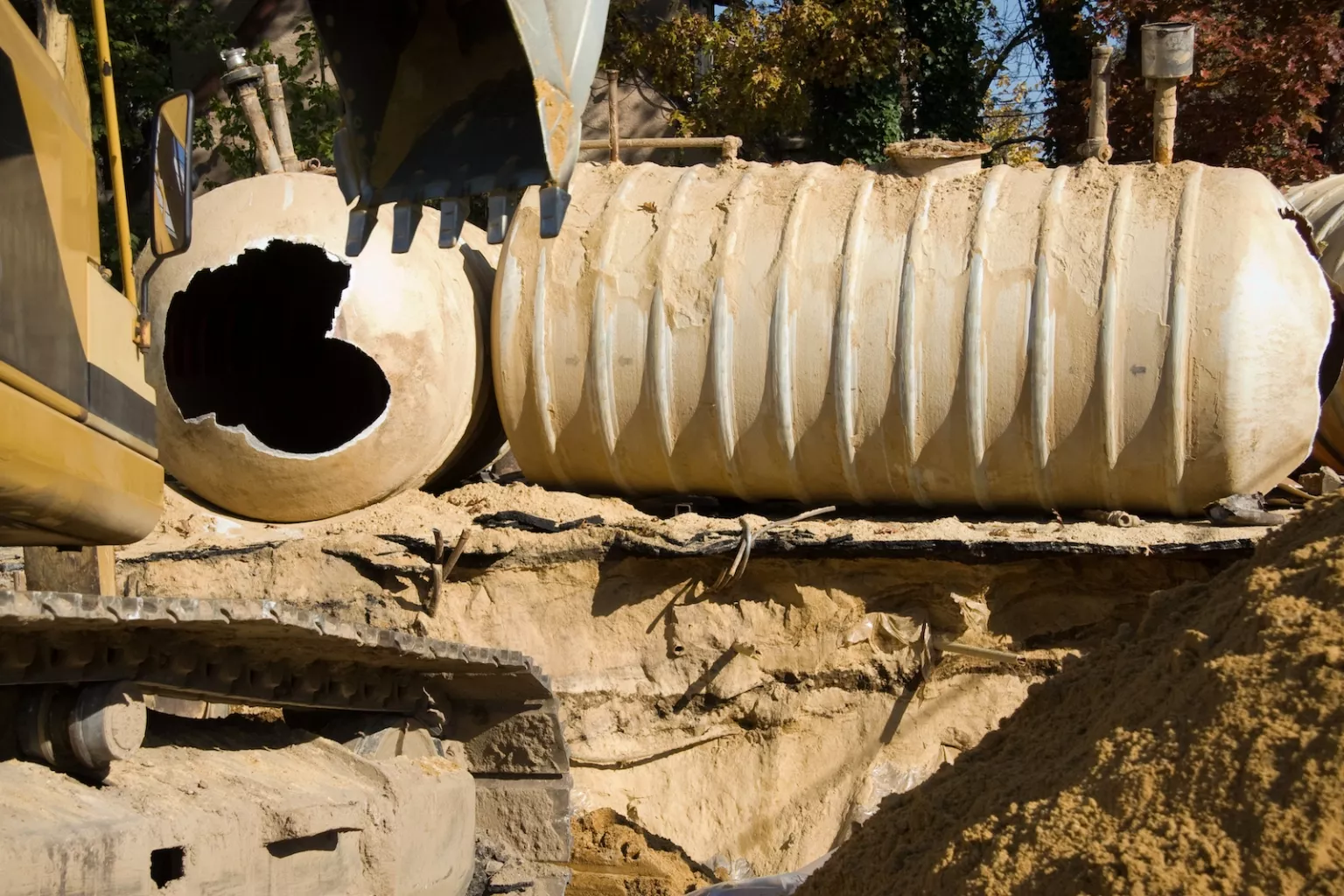 The claw of a backhoe digs out a large oblong structure from the ground.