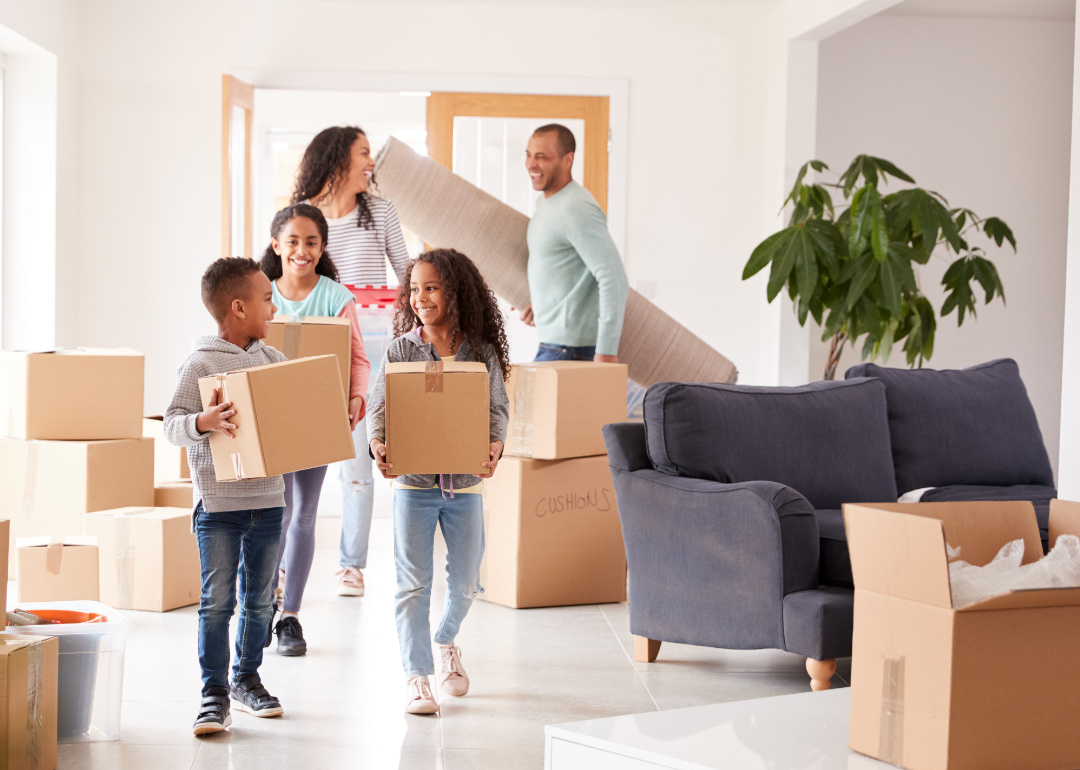 Parents and three children carry boxes into their home.