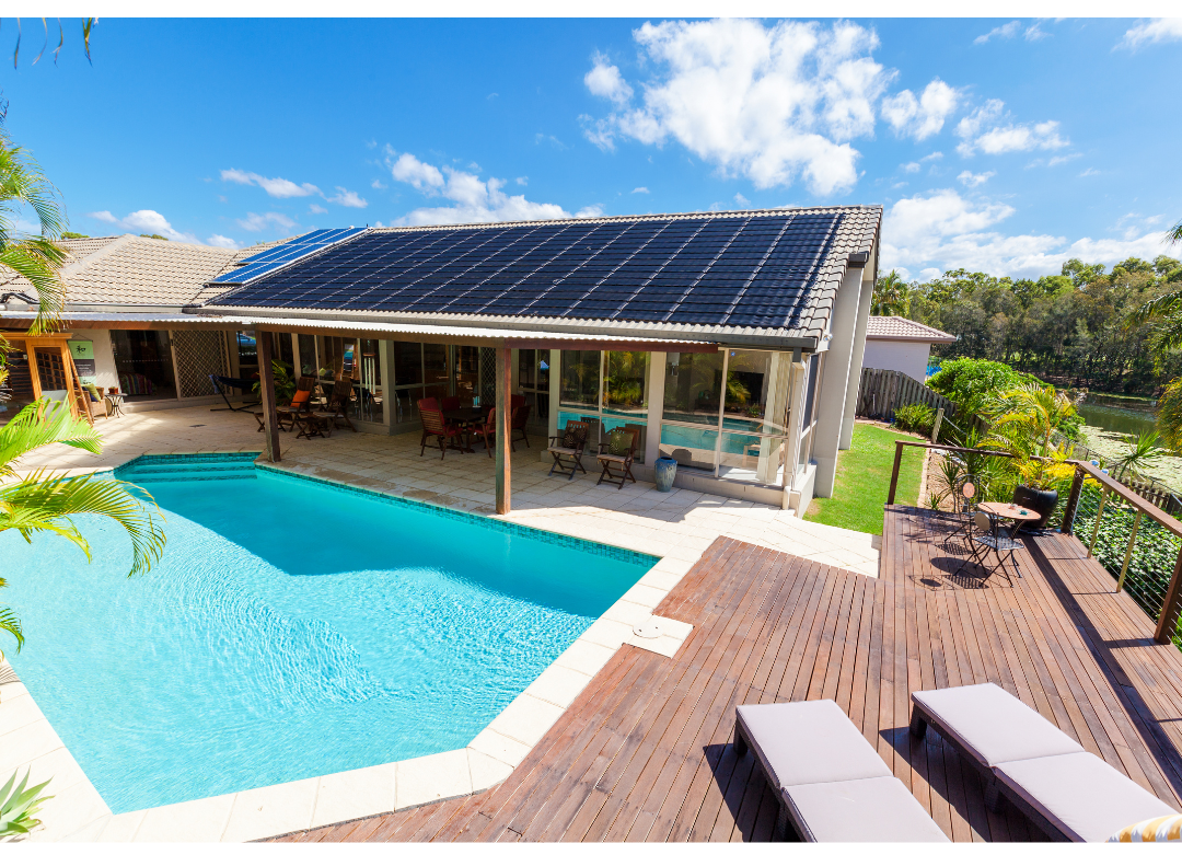 A swimming pool in a backyard with solar panels on the house beside it.