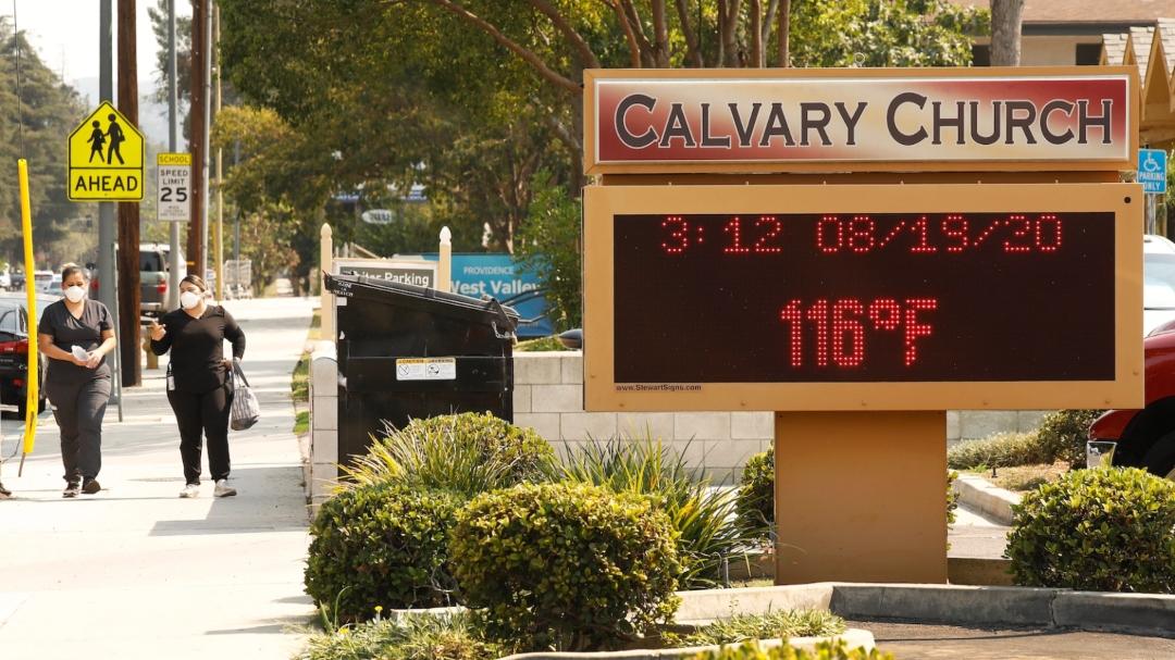 People walk past a church sign reading “116 degrees F.”