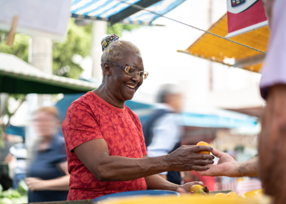 An older woman in glasses buys a piece of fruit at a farmers market