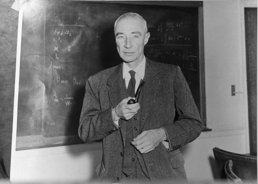 Robert Oppenheimer (1904-1967), American physicist, Director of the Manhattan project. Undated photograph, standing before blackboard, holding pipe.