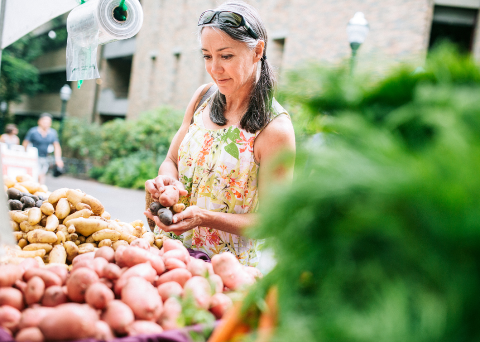 An older woman with gray hair buys potatoes at a farmers market
