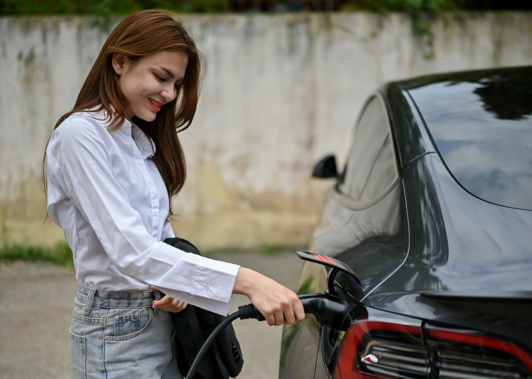 A woman is charging her black Tesla EV sedan.