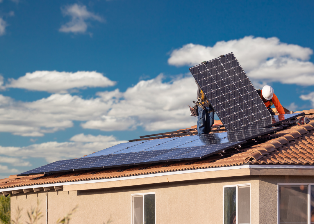 Workers installing solar panels on the roof of a house in the Southwest.