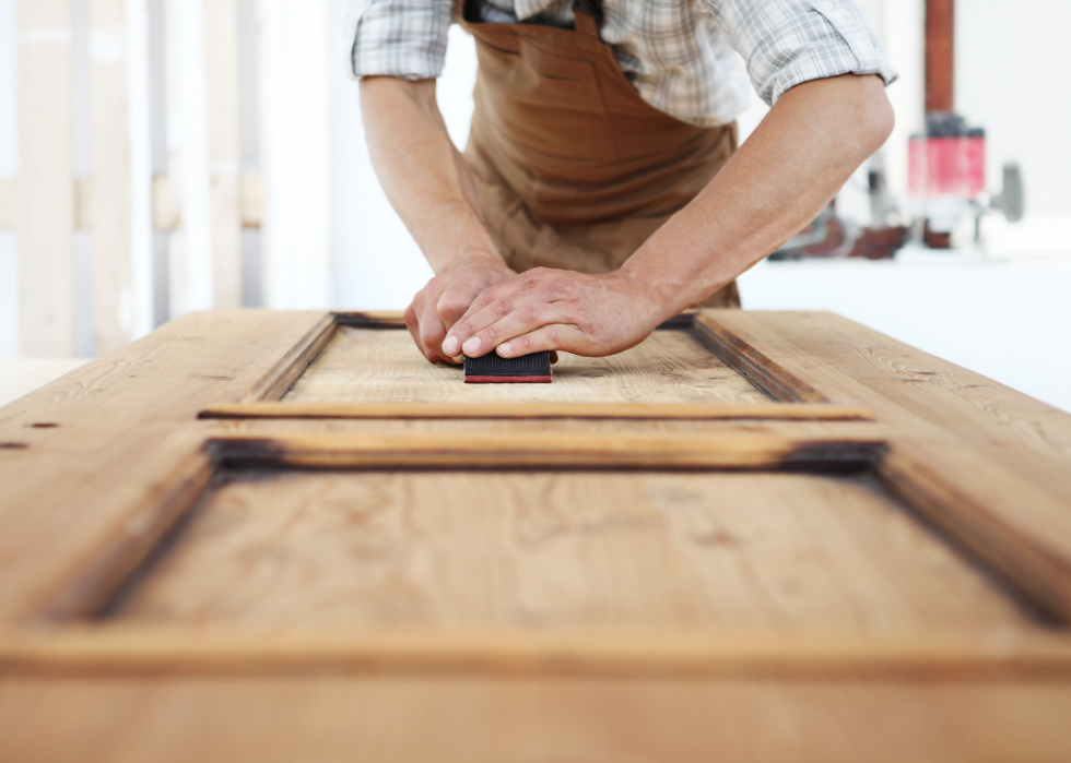 A furniture restorer sanding a large wood door