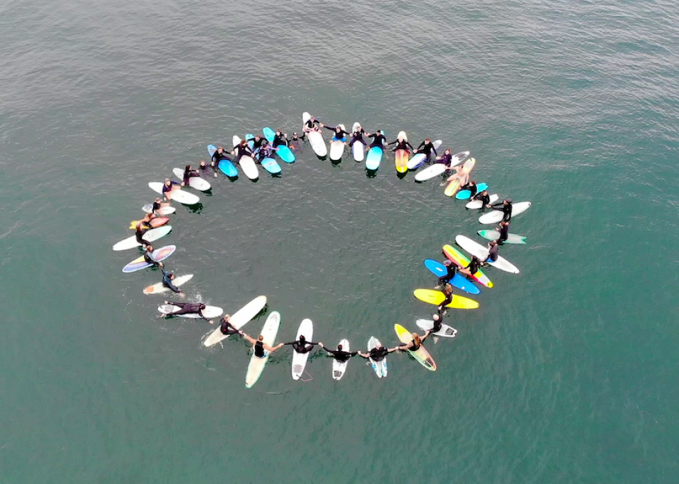 A group of surfers sit in a circle in the water on their boards