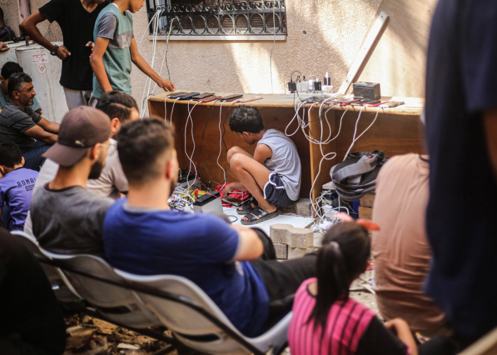 A Palestinian boy sits under the table inside the Al-Amal Hospital of the Palestinian Red Crescent Society to charge his mobile phone following the Israeli airstrike in Khan Yunis in the southern Gaza Strip. 