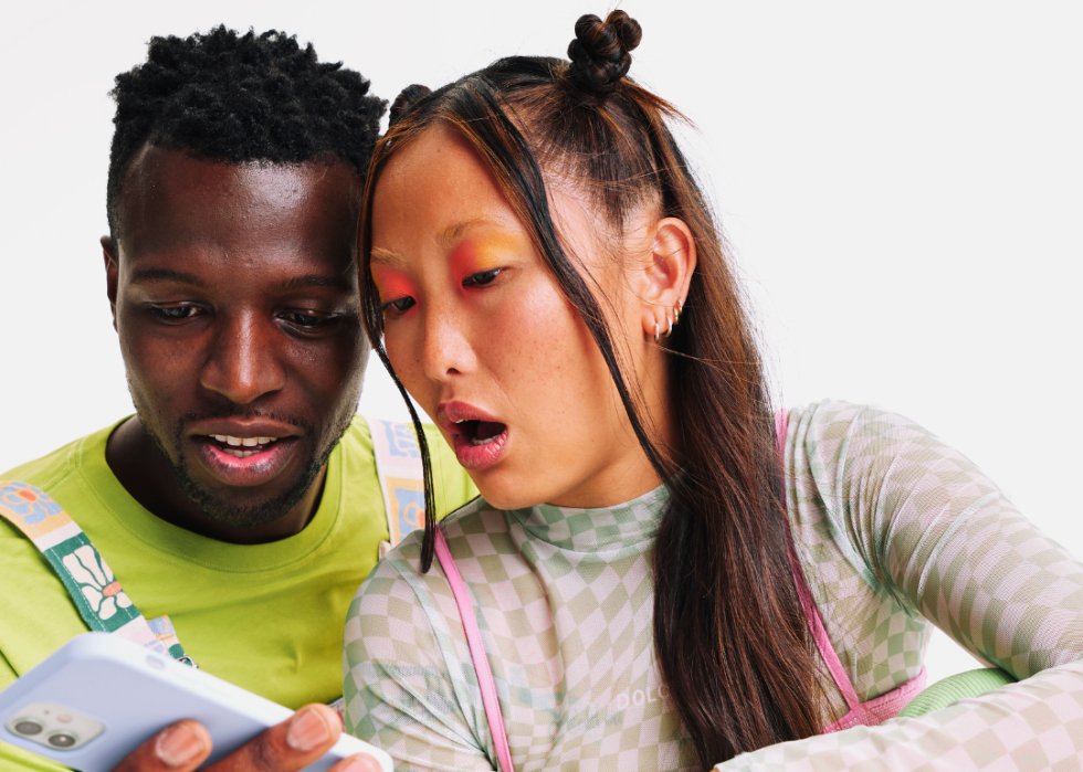 Woman with shocked expression looks at smartphone held by man.