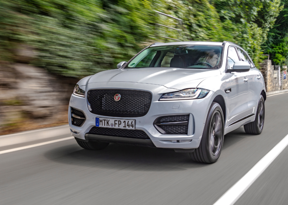 A man is driving new Jaguar F-Pace fast on a country road