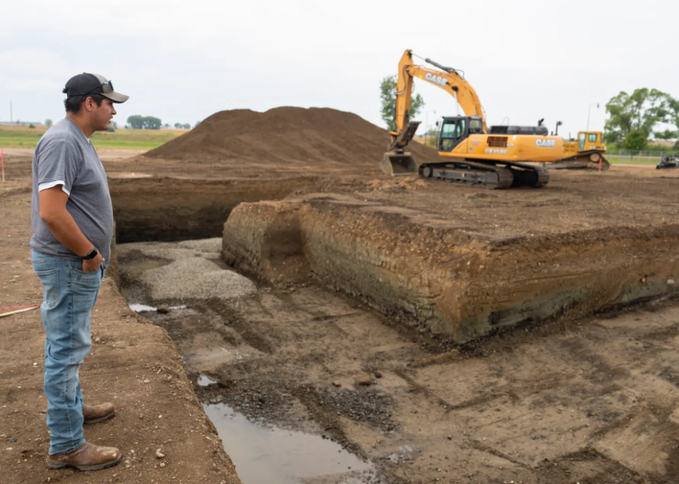 Joey Goodthunder looks at a foundation being dug with heavy machinery