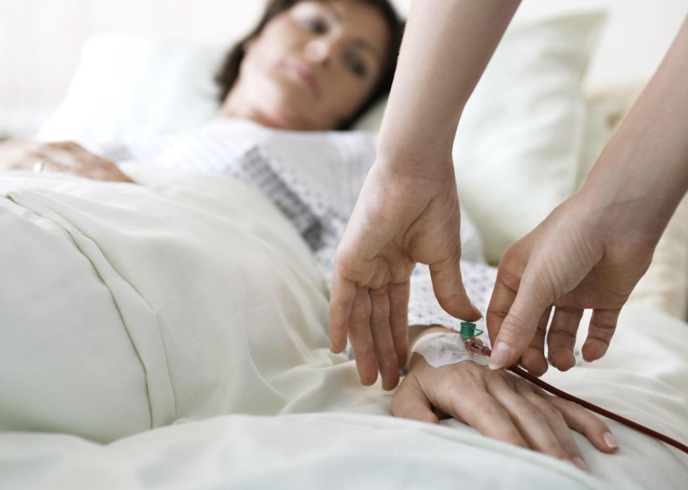 Close-up of hands attaching intravenous tube to patient's hand in hospital bed.