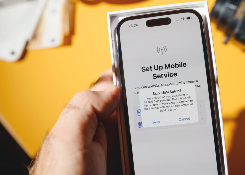 A hand holding an iPhone with a message on the screen that says, Skip eSIM setup?
