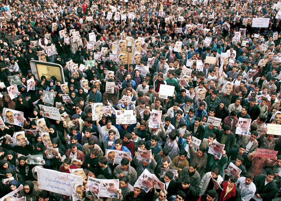 An overhead view of large crowds holding newspapers in the air. 