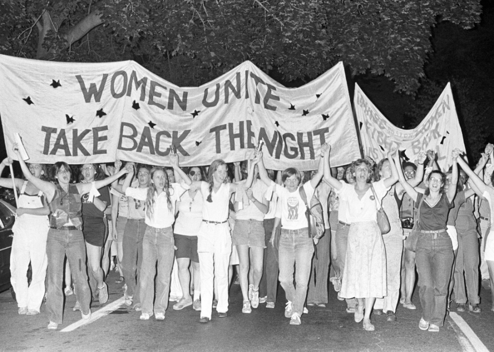 A group of women jointly hold up a banner that says Women Unite, Take Back the Night.