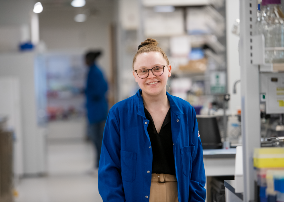 Madeline Szoo wearing a blue labcoat posing for a portrait in a lab. 