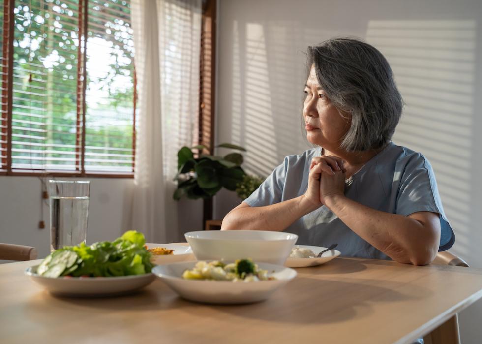 Senior Asian person sitting at their dining table but not eating.