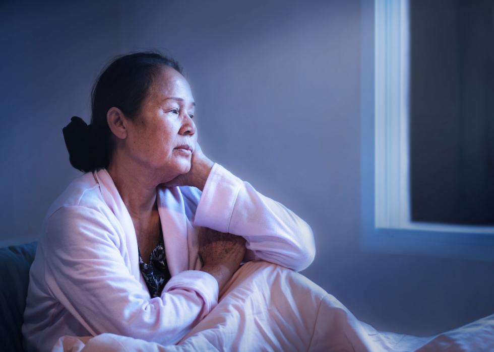 Asian senior awake in bed while it's still dark outside.