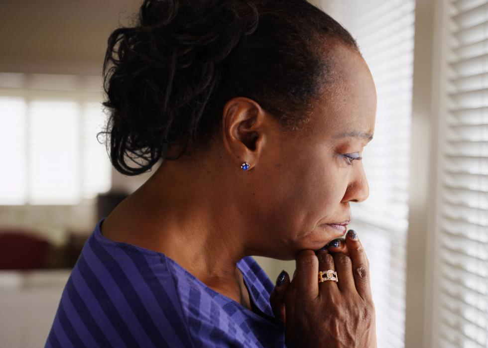 An older Black person mournfully looks out their window.