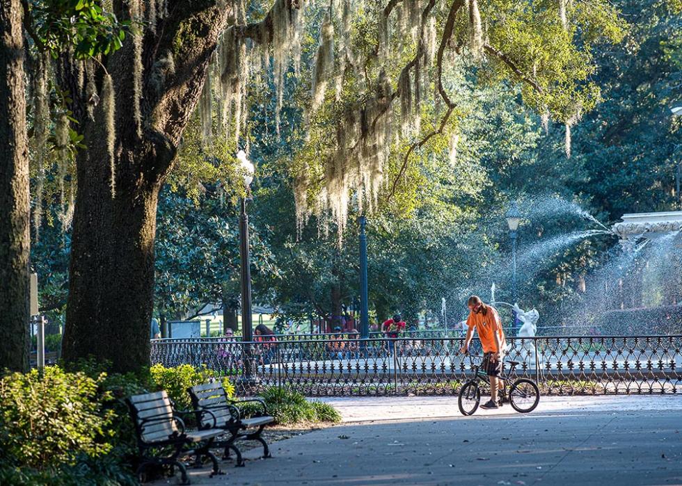 Forsyth Park fountain in Savannah, GA in October with a man in an orange shirt walking his BMX bike. 