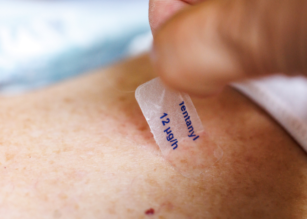 A woman removes a used fentanyl patch labeled "fentanyl 12 micrograms per hour."