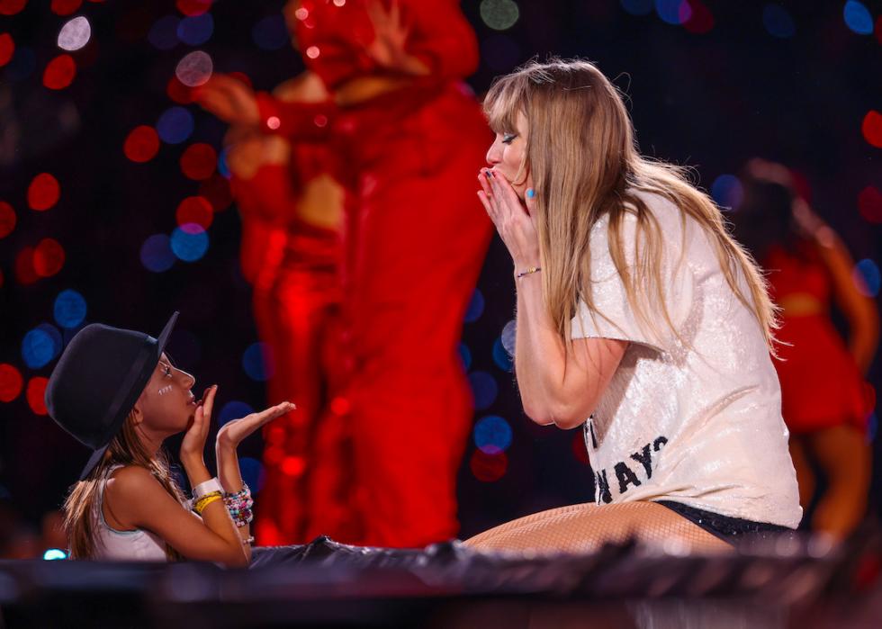 A young fan exchanges friendship bracelets with Taylor Swift as she performs onstage during The Eras Tour in 2023.