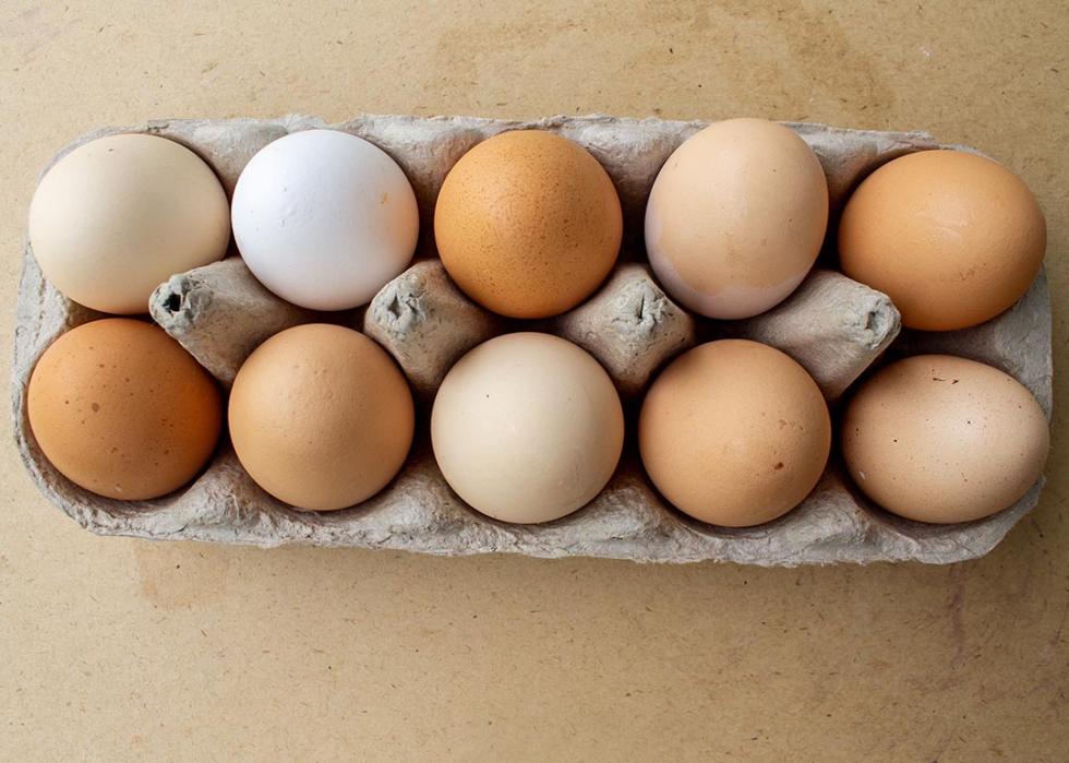 Top down view of a dozen eggs of varying colors from white to brown in a cardboard carton. 