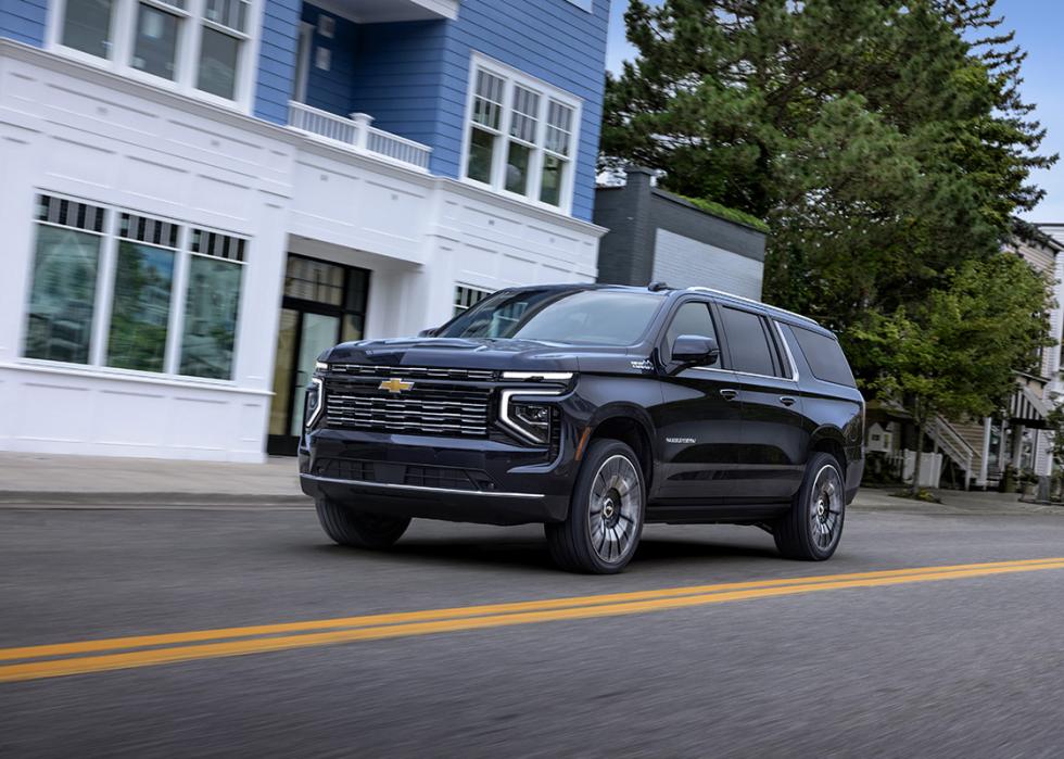 Dark Chevy Suburban driving past blue and white building on road.