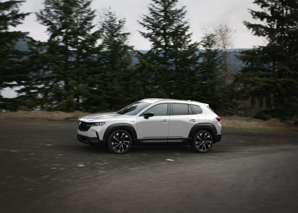 White Mazda CX 50 driving on a road in the forest.